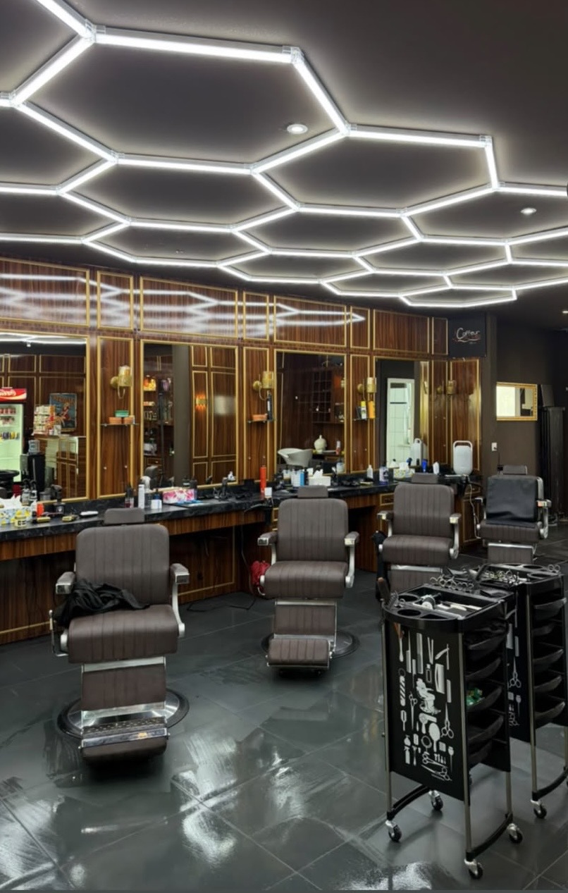Salon Coiffeur Leo mit Holzfronten, Goldrahmen, Spiegeln und Barberstühlen unter hexagonaler LED-Beleuchtung